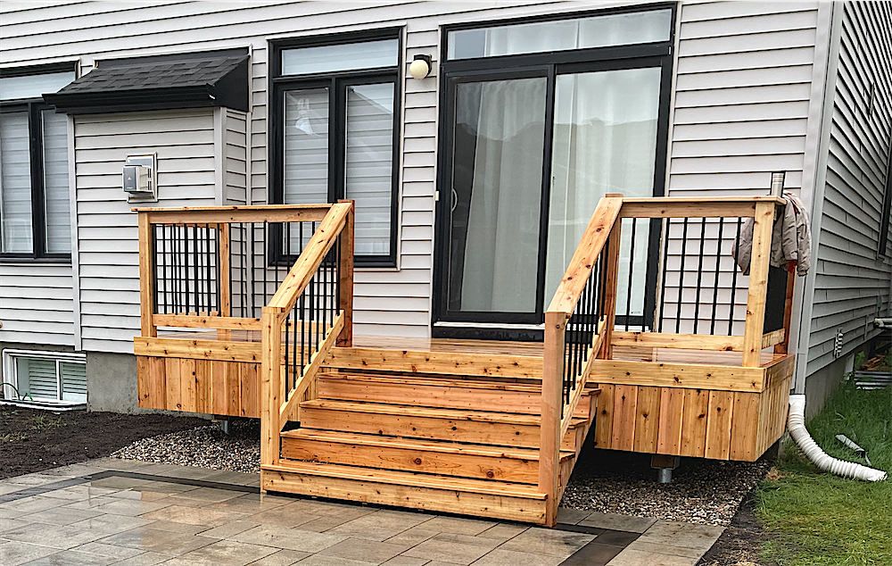 Small cedar deck with wide steps and black balusters at a sliding door, set on a paver landing