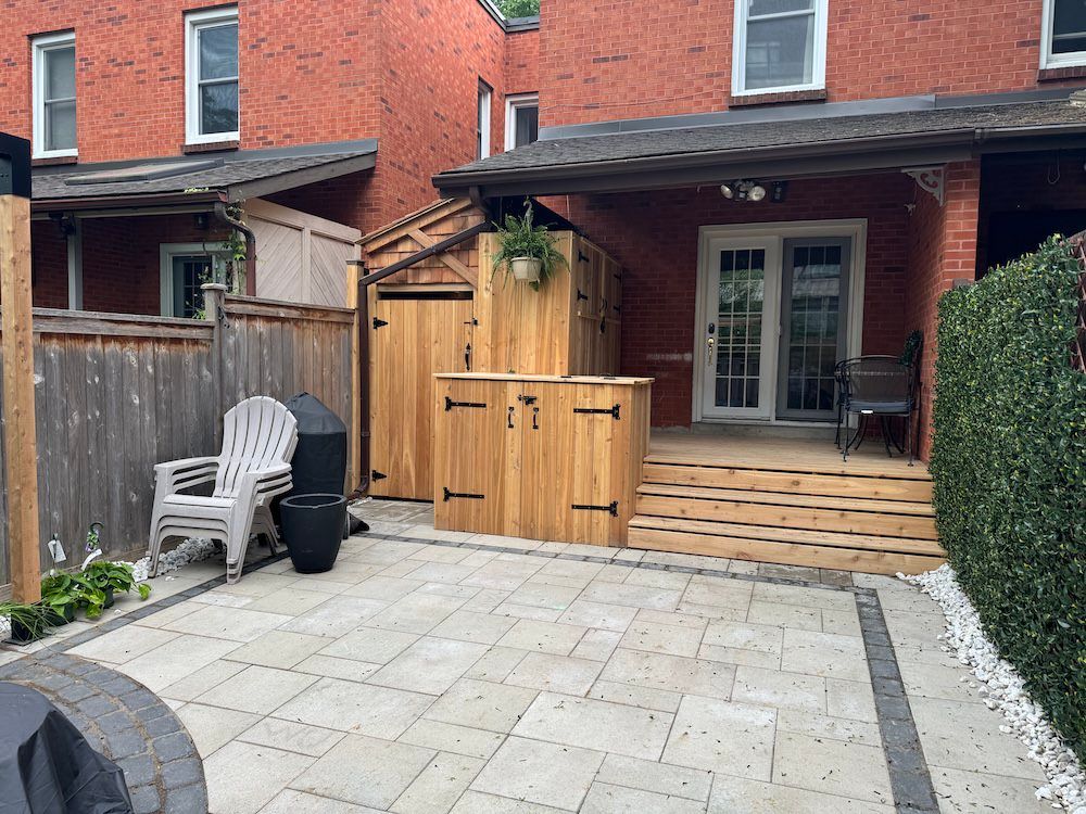 Small cedar deck with wide steps and a cedar storage enclosure with black hinges, next to a paver patio at the back of a brick house