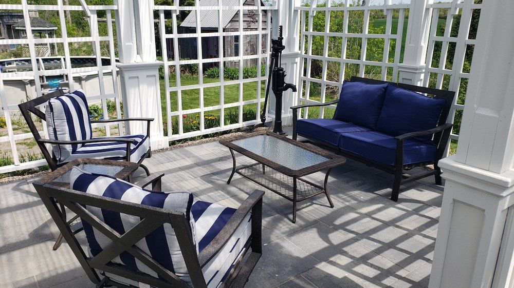 Patio seating under a white pergola with lattice panels, striped armchairs and a blue loveseat around a glass-top table