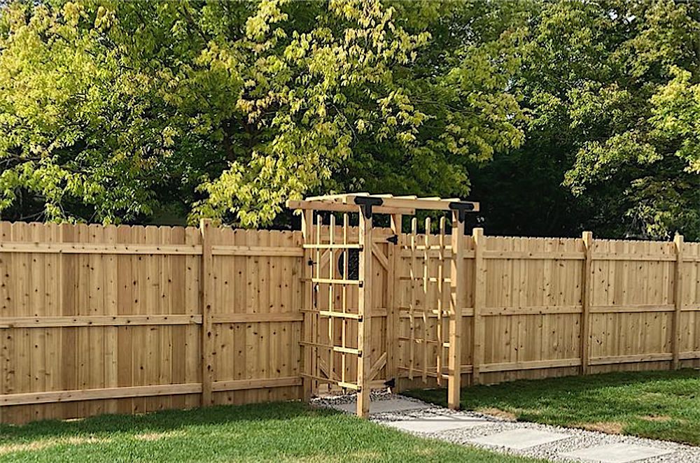 Cedar privacy fence along a lawn with a lattice gate framed by black brackets