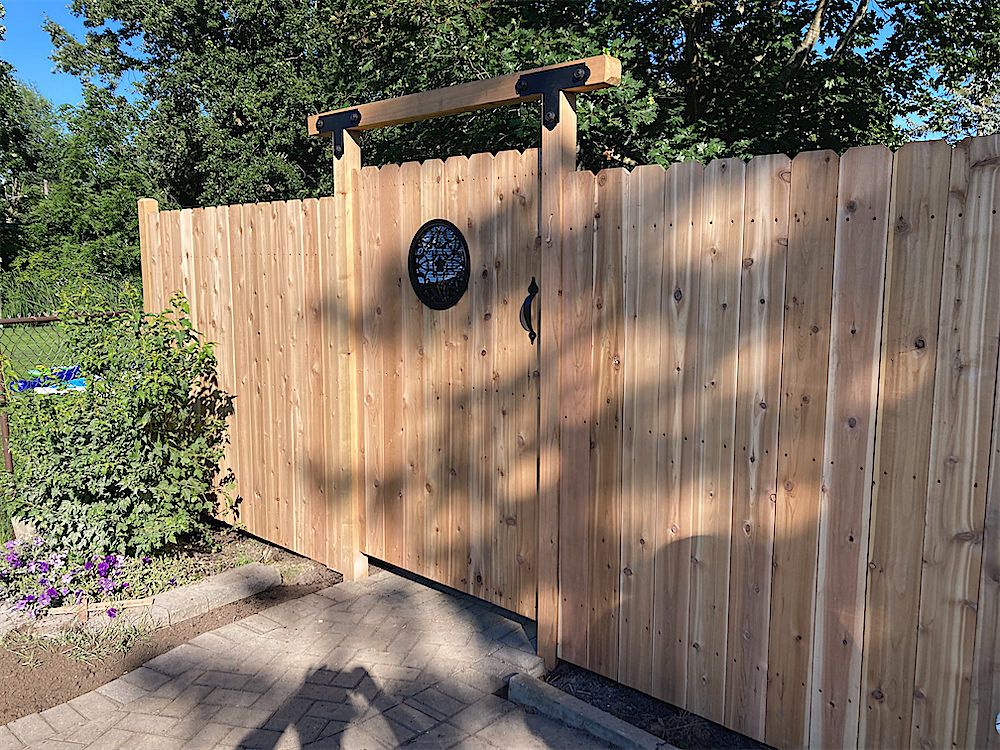 Tall cedar privacy fence and gate with black top brackets and a round decorative panel in the gate