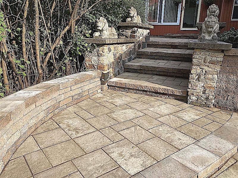 Curved stone seating wall and paver patio with wide steps up to a landing flanked by stone pillars and lion statues