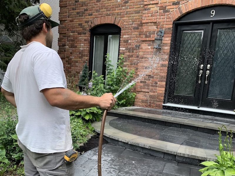 Curved stone front steps and landing at a brick house with a double black door, a man rinsing the stone with a hose