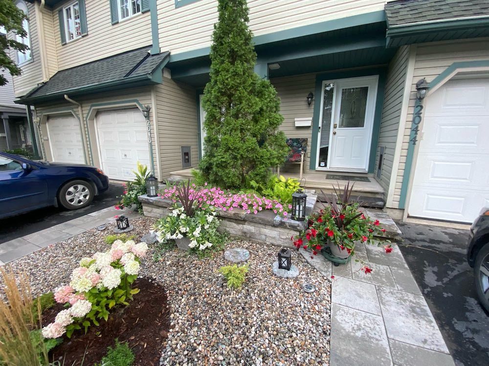 Paver walkway beside a front garden of flowering shrubs, perennials and gravel at the door of a townhouse