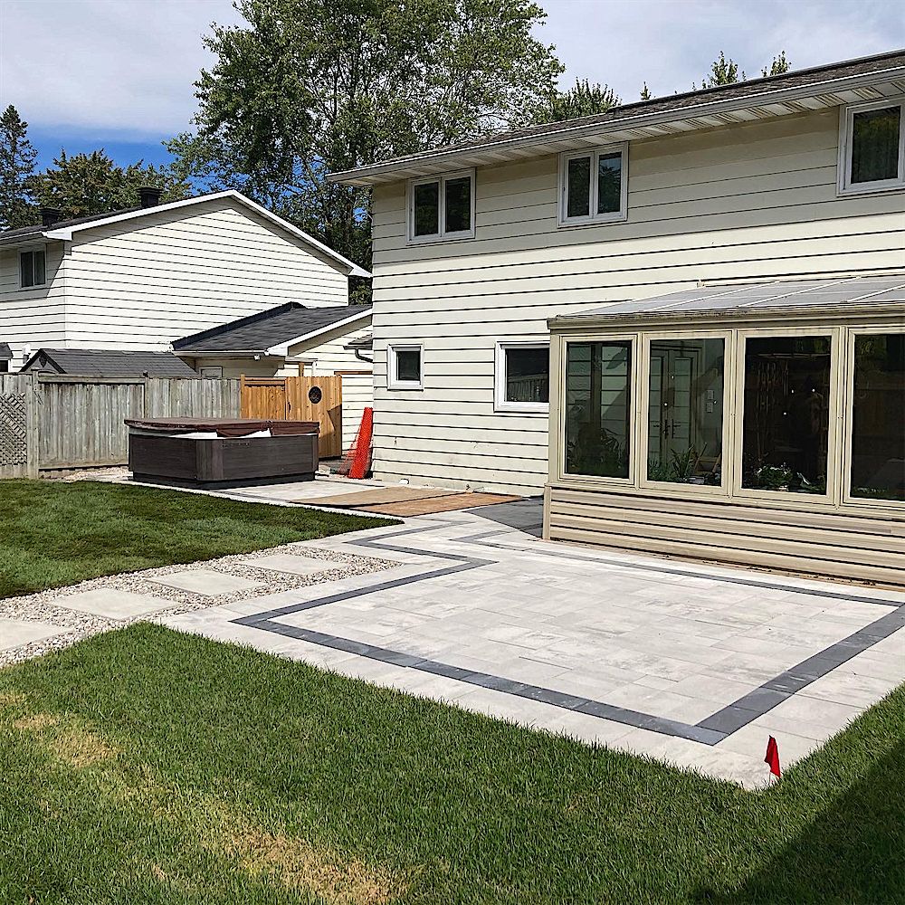 Light grey paver patio with a dark border set into a green lawn behind a two-storey house