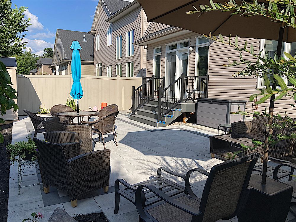 Light paver patio with a bistro table, wicker chairs and a patio umbrella outside the back doors of a two-storey house