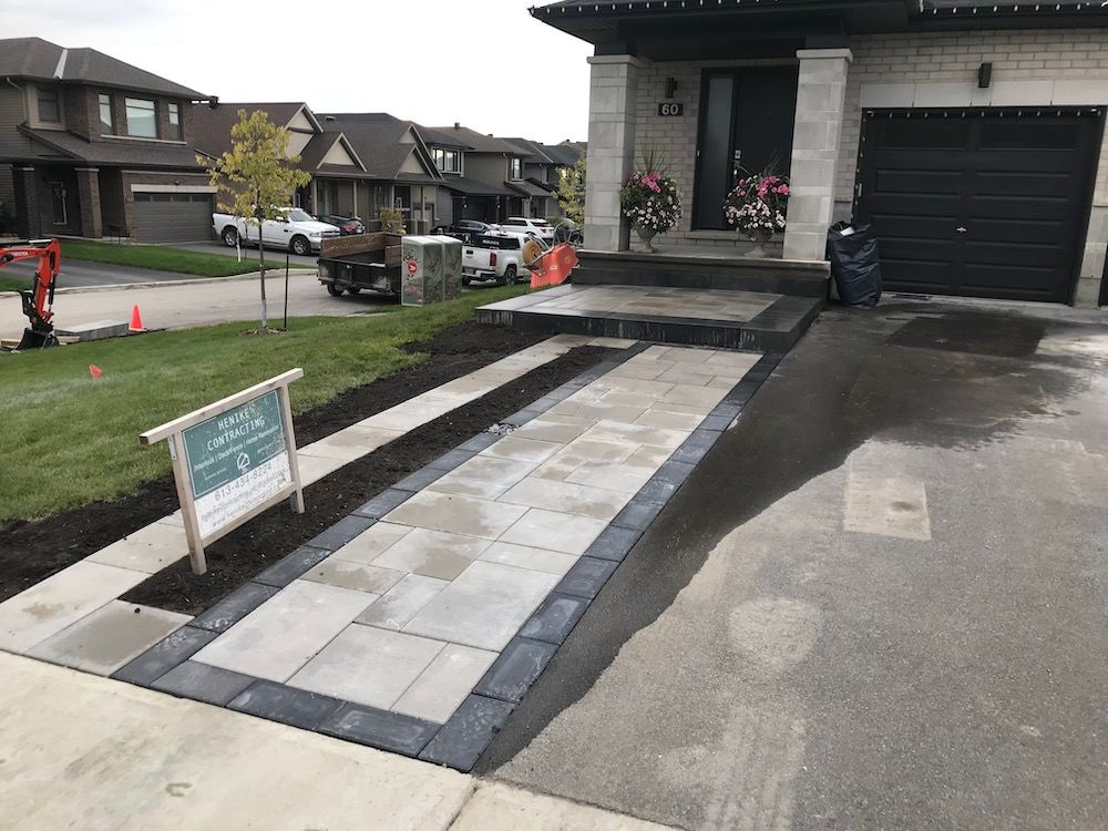New paver walkway with a dark border running from the sidewalk to a front door, grass and soil on both sides