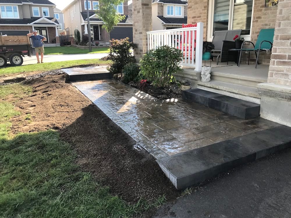 Dark paved walkway with a wide dark step up to a porch, bare soil beside it