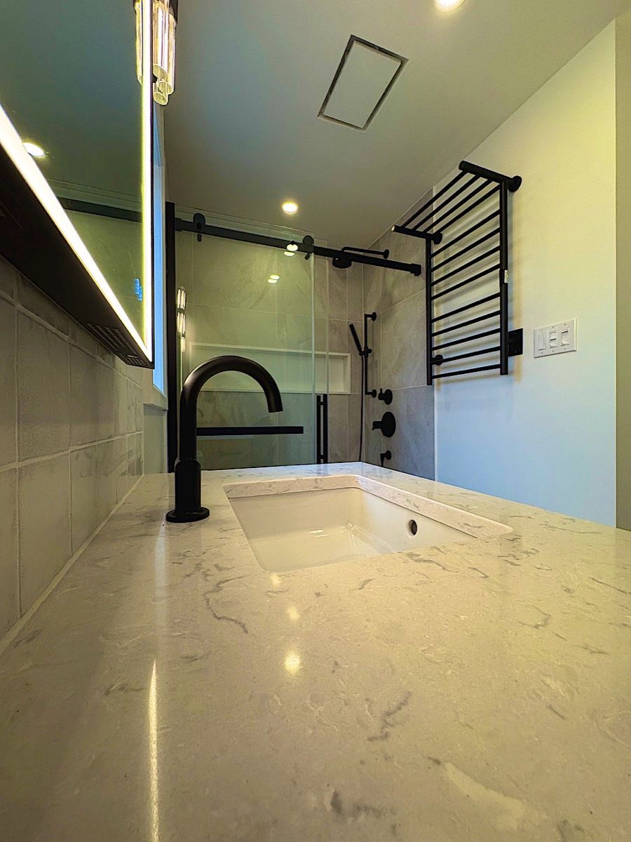 Bathroom counter with a white undermount sink, a tall black faucet, a lit mirror and a black towel rack