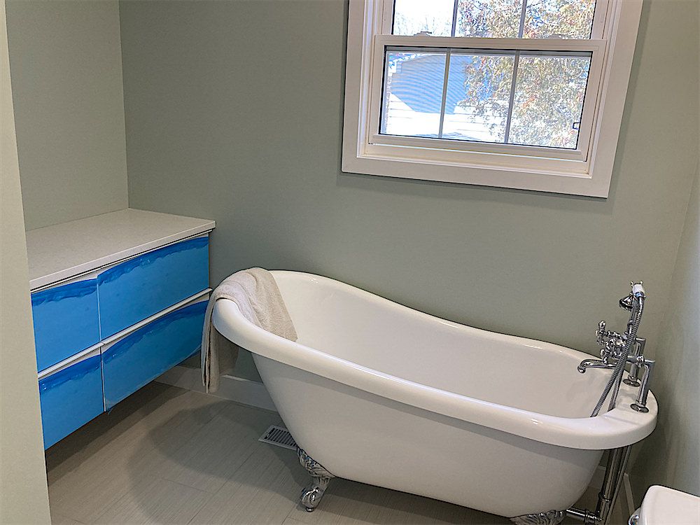 Bathroom with a clawfoot tub, a white vanity with protective blue film on the drawers and a window above the tub area