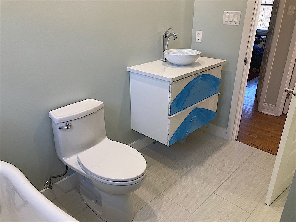 Bathroom with a floating white vanity covered in blue protective film, a vessel sink, a toilet and light floor tile