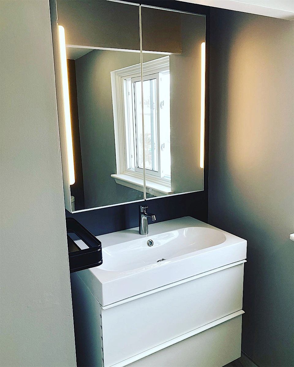 Small bathroom with a white floating vanity under a mirrored cabinet with lit sides, dark wall paint and a window