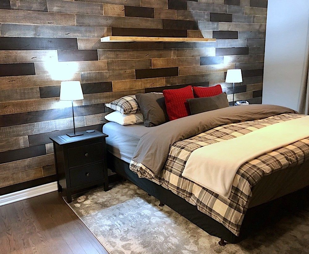 Bedroom with an accent wall of mixed-width dark and weathered wood planks, a floating shelf and a made bed