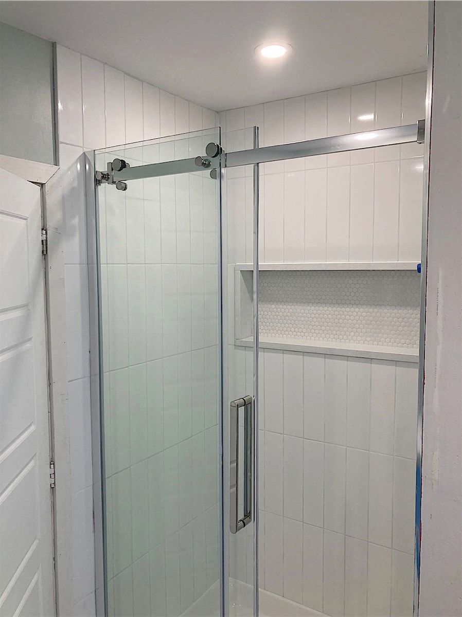 Walk-in shower with white tile and a glass sliding door with a chrome pull handle