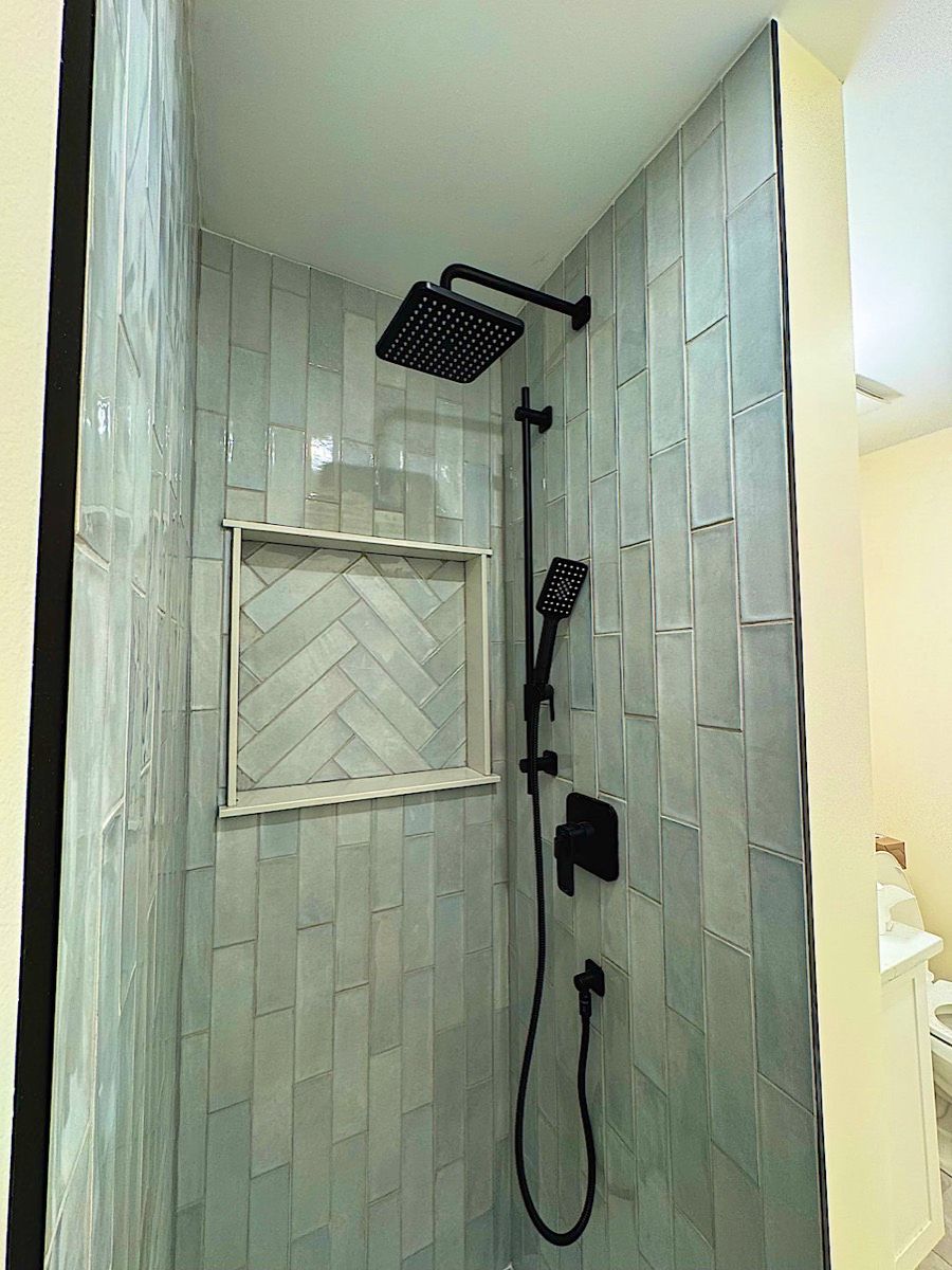 Tiled shower with a herringbone-pattern niche, a black rain head, a black hand shower and pale green vertical tile