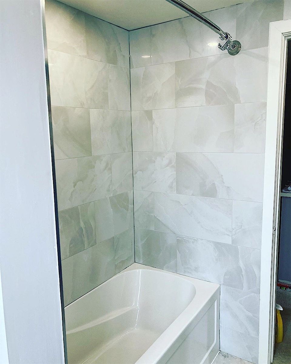 Bathtub and shower wall finished in large marble-look tile with a rain shower head and a glass edge